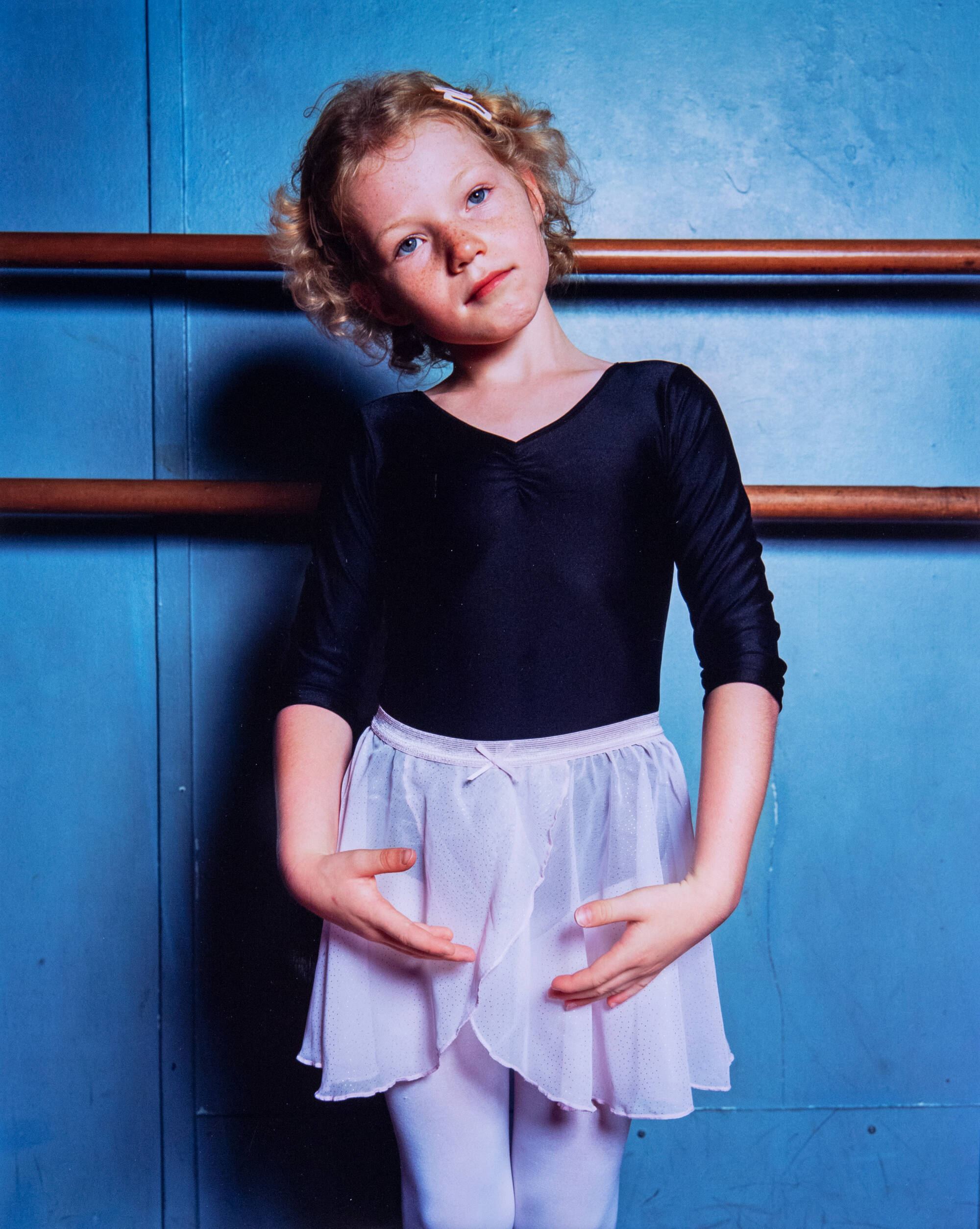 Color photograph of a child wearing ballerina clothing against a blue wall.